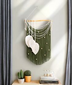 a green wall hanging with two white hearts on it next to a potted cactus