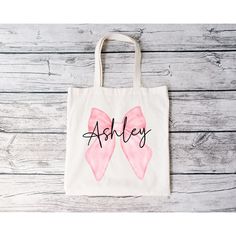 the personalized pink bow tote bag is shown on a wooden table with wood planks