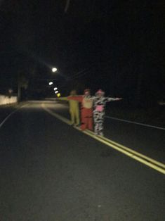 three people standing on the side of a road at night with their arms in the air