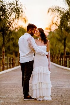 a bride and groom standing together in the middle of an empty road at sunset with trees in the background