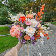 a bouquet of flowers is being held up by someone's hand in the park