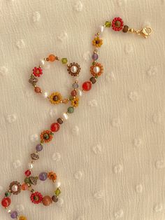 a beaded necklace with flowers and pearls on it sitting on a white cloth covered surface