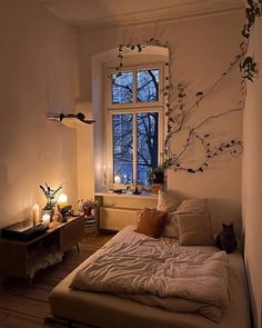 a bed sitting under a window next to a night stand with two candles on it