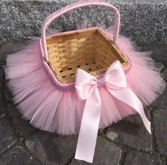 a basket with a pink tutu and a bow on the front sitting on a stone floor