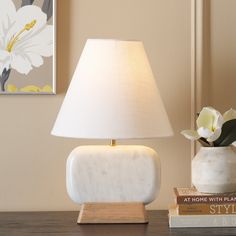 a white lamp sitting on top of a table next to a book and a vase