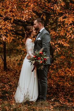 a bride and groom standing in front of a tree with fall leaves on the ground