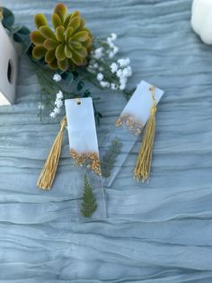 two tags with tassels are sitting on a table next to flowers and a vase