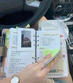 a person's hand is holding a pen and writing on a notebook in their car