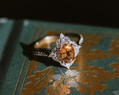 an orange and white diamond ring sitting on top of a green tablecloth with gold foil