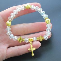 a hand holding a gold cross and crystal beaded bracelet