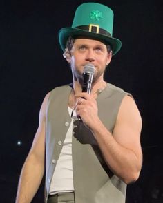 a man wearing a green hat holding a microphone in his right hand while standing on stage