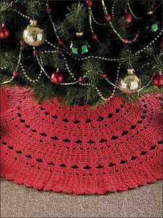 a crocheted christmas tree skirt sitting next to a christmas tree with ornaments on it