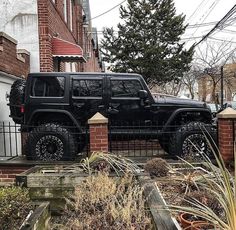 a black jeep parked on the side of a road next to a brick wall and fence