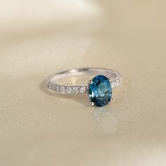 a ring with a blue topaz stone and diamonds on the bottom is sitting on a white surface