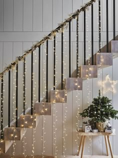 stairs decorated with christmas lights next to a table and potted plant on the floor