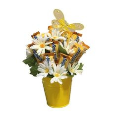 a yellow vase filled with lots of white flowers and candy bars on top of it