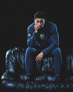 a man sitting on top of a black leather couch in front of a dark background