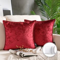 two red velvet pillows sitting on top of a white couch next to a green plant