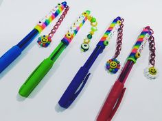 several different colored pens are lined up on a white surface with smiley faces and beads attached to them