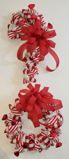 two red and white wreaths hanging on the wall next to each other with ribbons tied around them