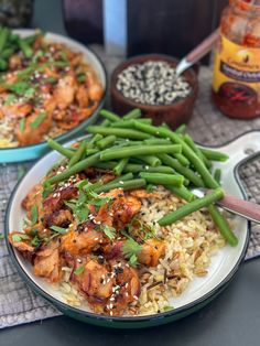 two plates filled with chicken and rice covered in sesame seeds, garnished with green beans