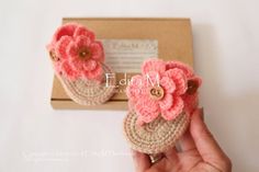 a hand holding a pair of crocheted baby shoes in front of a box