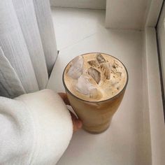 a person holding a drink with ice on the table next to a window sill