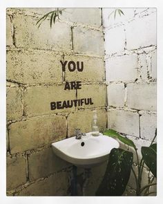 a white sink sitting next to a wall with graffiti on it's side and the words you are beautiful above it