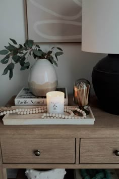 a wooden table topped with a candle and some beads on top of it next to a vase