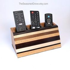 three remote controls sitting on top of a wooden holder with two different types of remotes