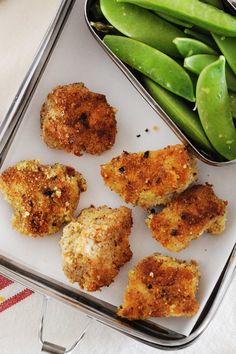 several pieces of fried food in a metal container next to green beans and snap peas