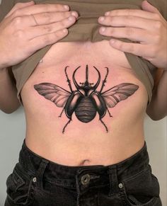 a woman's stomach with a black beetle tattoo on her belly and hands behind her back