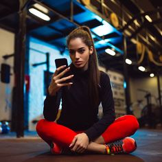 a woman sitting on the floor with her phone in her hand and looking at it