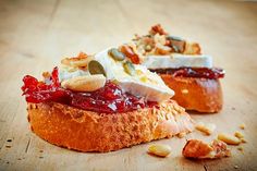 two pieces of bread with fruit and nuts on them sitting on a wooden table next to another piece of bread