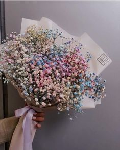 a person holding a bouquet of flowers on top of a white paper bag with pink, blue and purple flowers