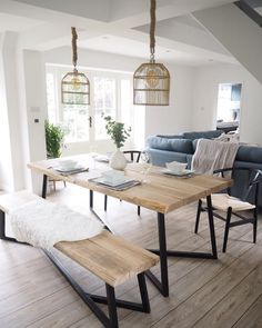 a dining room table with two benches in front of it and a couch behind it