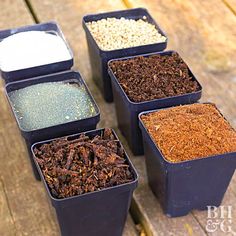 four black containers filled with different types of dirt and grains on top of a wooden table