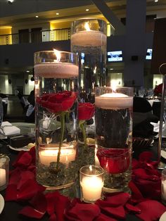 candles and roses in glass vases on a table with red rose petals around them