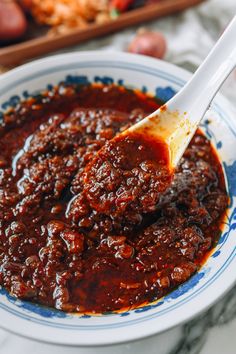 a spoon full of chili sauce sitting on top of a white and blue plate with red peppers in the background