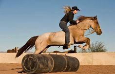 a woman riding on the back of a white horse next to a barrel and barrels