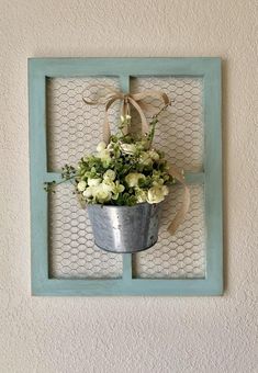 a metal bucket filled with flowers on top of a wall next to a blue frame