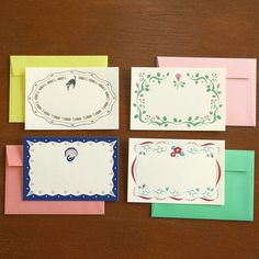 four cards with different designs on them sitting on top of a wooden table next to envelopes