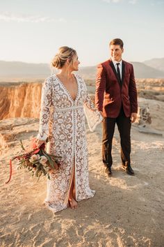 a bride and groom holding hands while standing on top of a hill in the desert