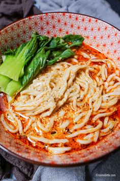 a bowl filled with noodles and vegetables on top of a tablecloth next to a napkin