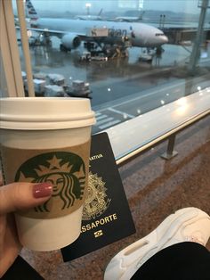 a person holding up a starbucks cup in front of an airport