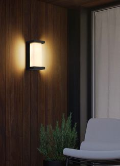 a wall light that is on the side of a wooden wall next to a chair and potted plant