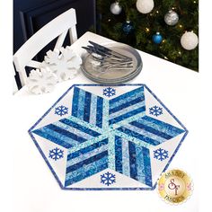 a white table topped with a blue and white snowflake placemat next to a christmas tree