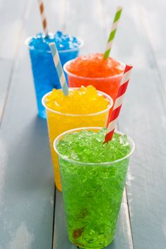 three different colored drinks sitting next to each other on top of a wooden table with straws