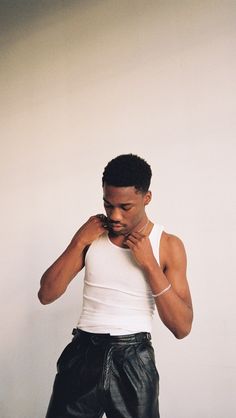 a man in white tank top and black leather shorts standing with his hands on his chin