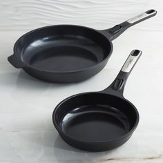 two black frying pans sitting next to each other on a white counter top